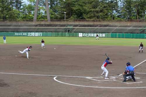 マウンドからボールを投げる男性、バットを持って構えている男性、内野や外野を守っている選手と、キャッチャーの後ろに立っている審判がいる試合中の写真