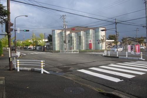 手前に横断歩道、奥に白い建物が写っている交差点の写真