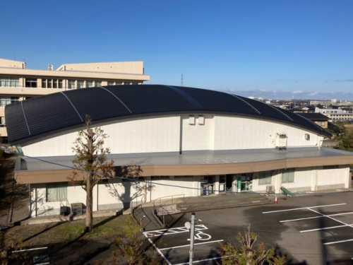 黒い屋根の体育館の外観と駐車場を上空から撮影した写真