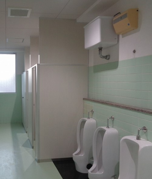 男子トイレ側改装後の様子。床は塩ビシートが貼られており、奥に個室が2つ、手前に小用便器が3つある。