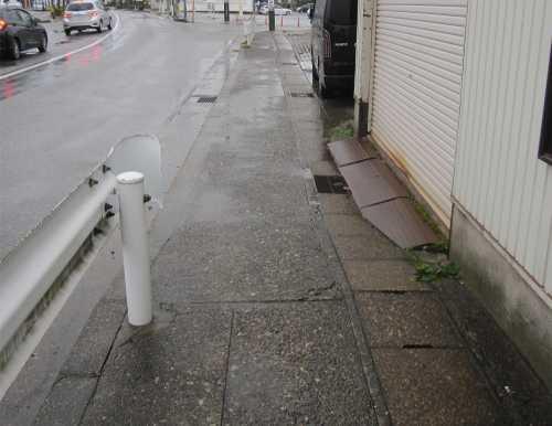 雨に濡れたアスファルトの道路の地面が写っている改修前の写真