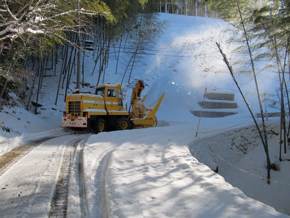雪が20センチメートルほど積もっている山間部の道路をロータリ型除雪車で除雪中。