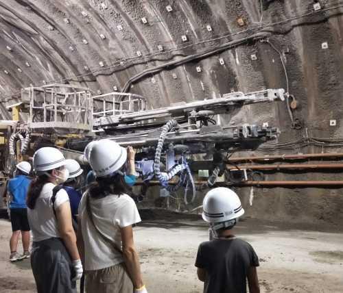ヘルメットを被った生徒達が、施工中の月浦トンネル内を見学している写真