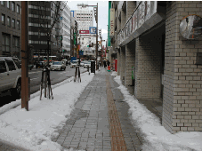 点字ブロックがある歩道の左右に雪が山積みになっている写真