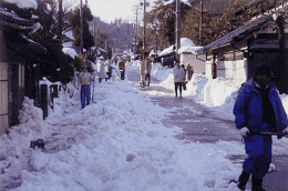 市民がスコップを持って道路の雪かきをしている写真