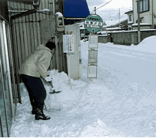 バス停に積もった雪を雪かきする市民の写真