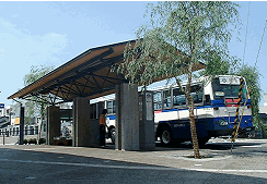 両脇に2本の木が植えられ、屋根のあるバス停にバスが停車している橋場町バス停 の写真