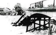 濁流の中、橋の左側が決壊し、壊れた部分がむき出しになっている様子の白黒写真