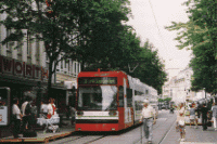 人々が行き交う市街地の路上を走る、赤色の車体の路面電車の写真