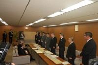 締結式で関係者の人達が直立しソファーの関係者2名と対面している写真