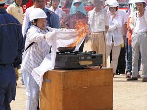 台に設置されたガスコンロの上で燃えている鍋に白い布をかけている女性の写真