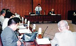 前の席にいる男性が立って話している様子を横に設置されている席で資料を見ながら聞いている金沢子ども条例（仮称）検討会議の写真