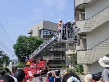 消防車のはしごに消防隊員3名が乗っていて、下から参加者たちが見ている写真