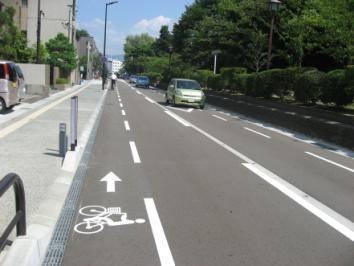 右側に木々がある大手町の道路に自転車と進行方向の矢印が書かれた写真