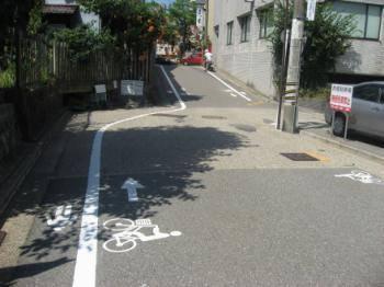ゆるやかな坂道の手前のカーブに自転車と進行方向の矢印が書かれた写真