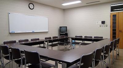 中央を四角く囲むように、長い机と椅子が並べられ、奥にホワイトボードが見える第2研修室の写真
