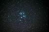 夜空に昇る青く輝く星や小さな白い星から連なるプレアデス星団（すばる）を撮影した写真