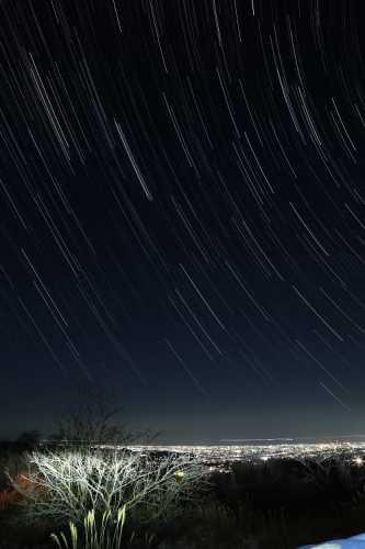 遠くに見える金沢の街並みの明かりの頭上に弧を描く星の軌跡の写真