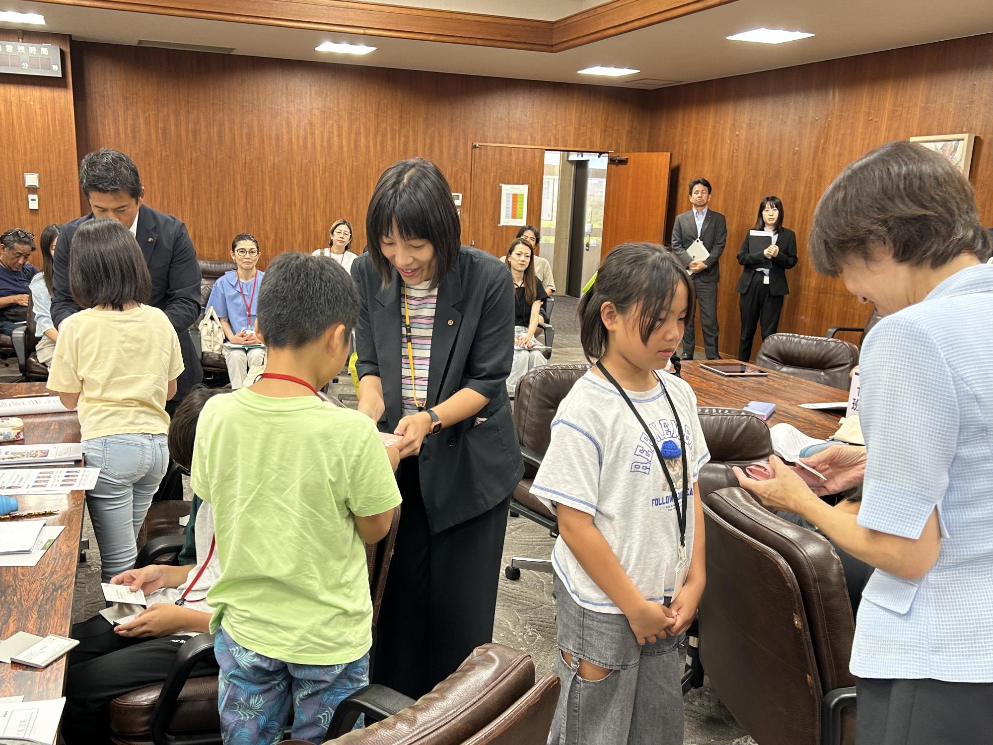 議会室内で議員と子ども議員が名刺交換をする写真