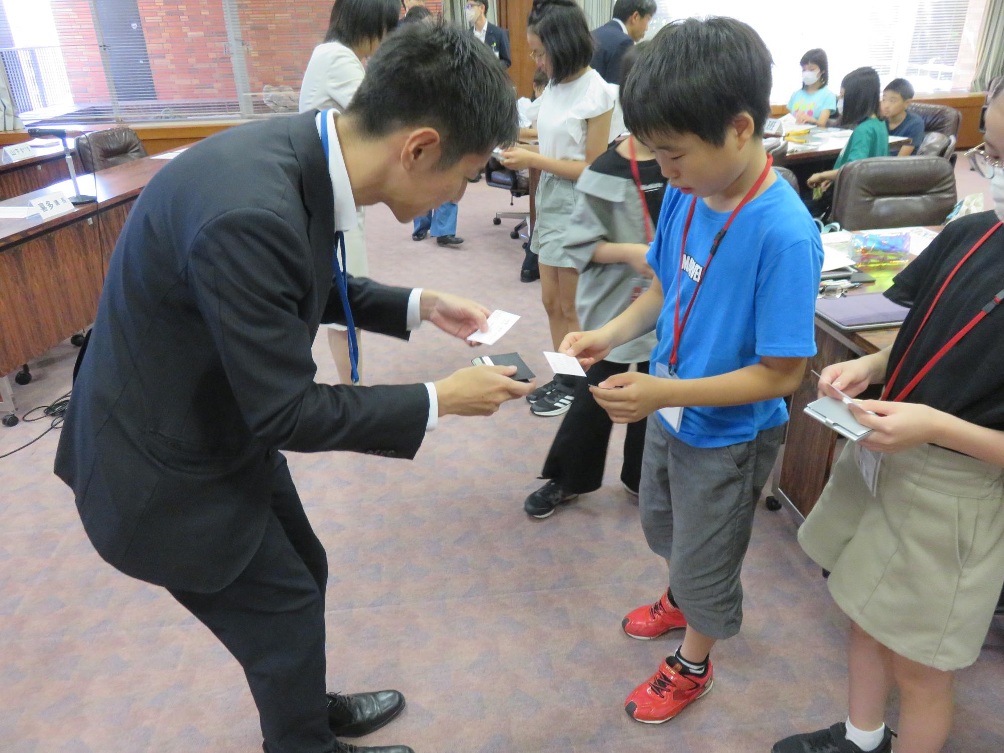 議会室内で議員と子ども議員が名刺交換をする写真