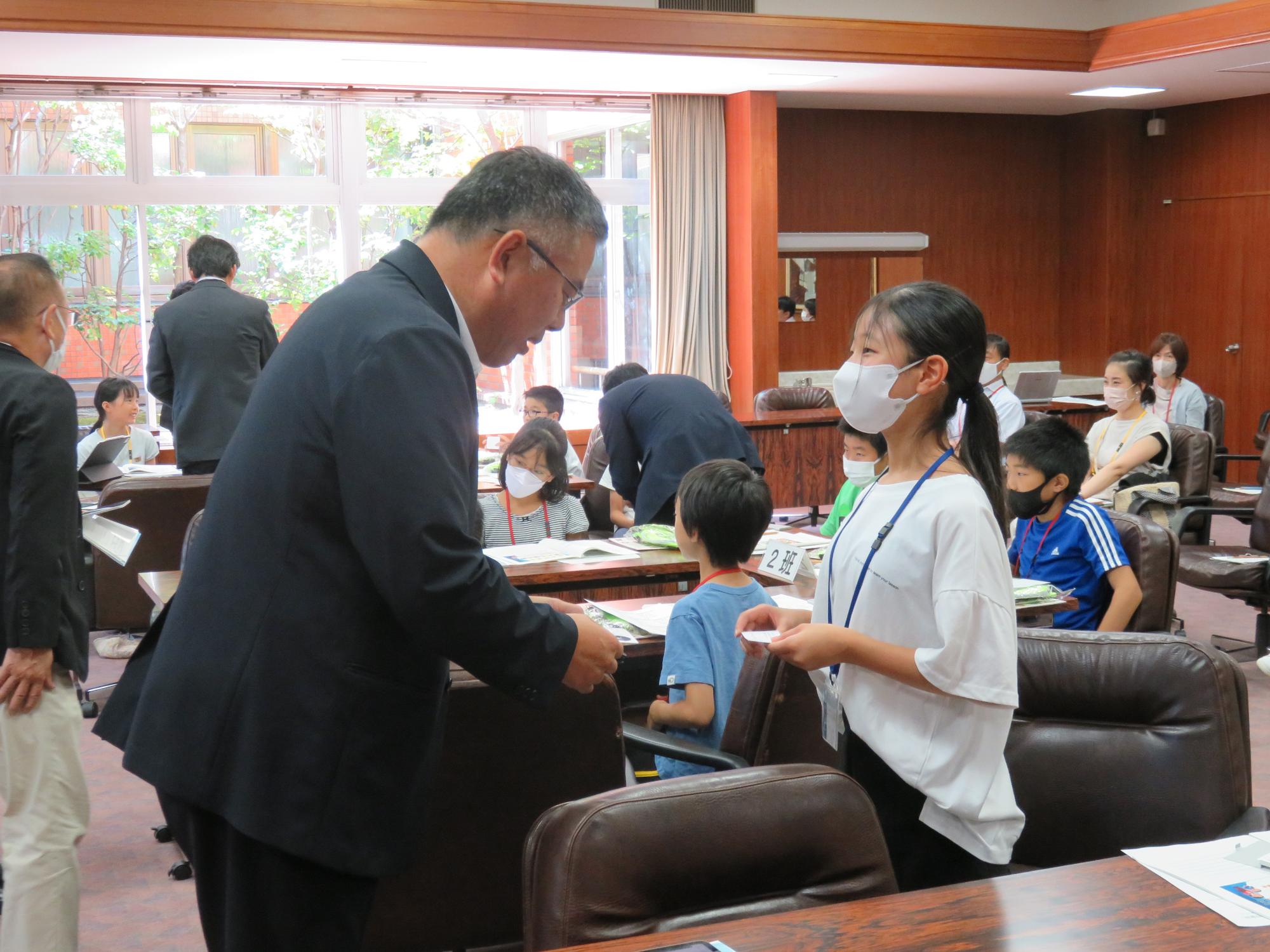 議会室内で議員と子ども議員が名刺交換をする写真