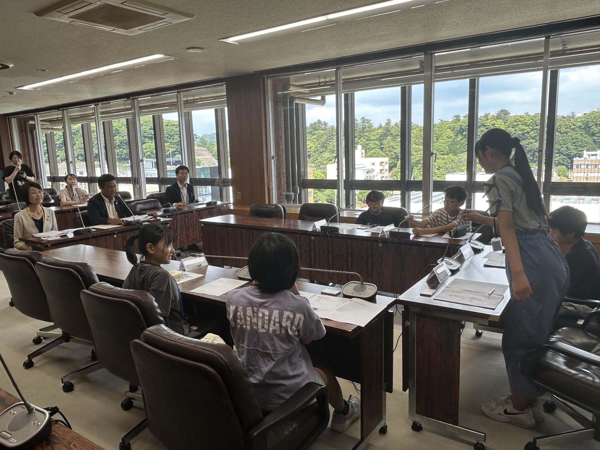 会議室にコの字に設置された長机の椅子に座っている子供たちが議員体験を行っている様子の写真